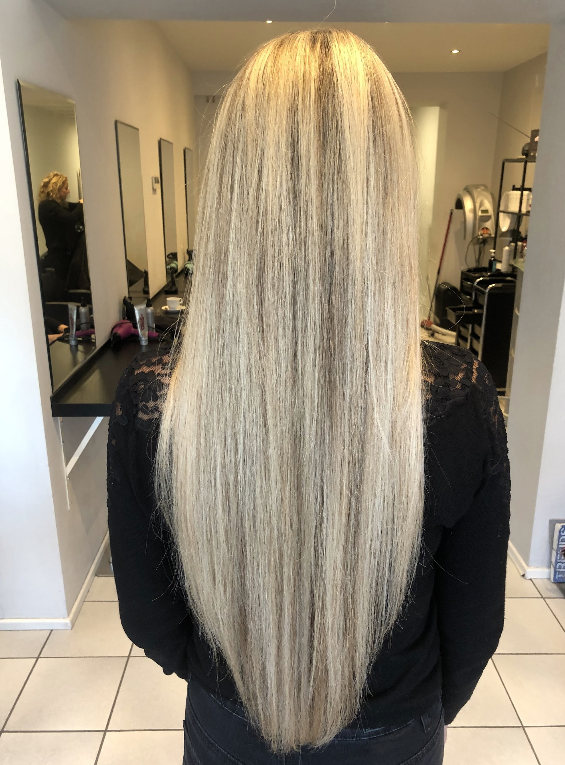 Lang, steil blond haar van achteren gezien in de salon, met de spiegels op de achtergrond