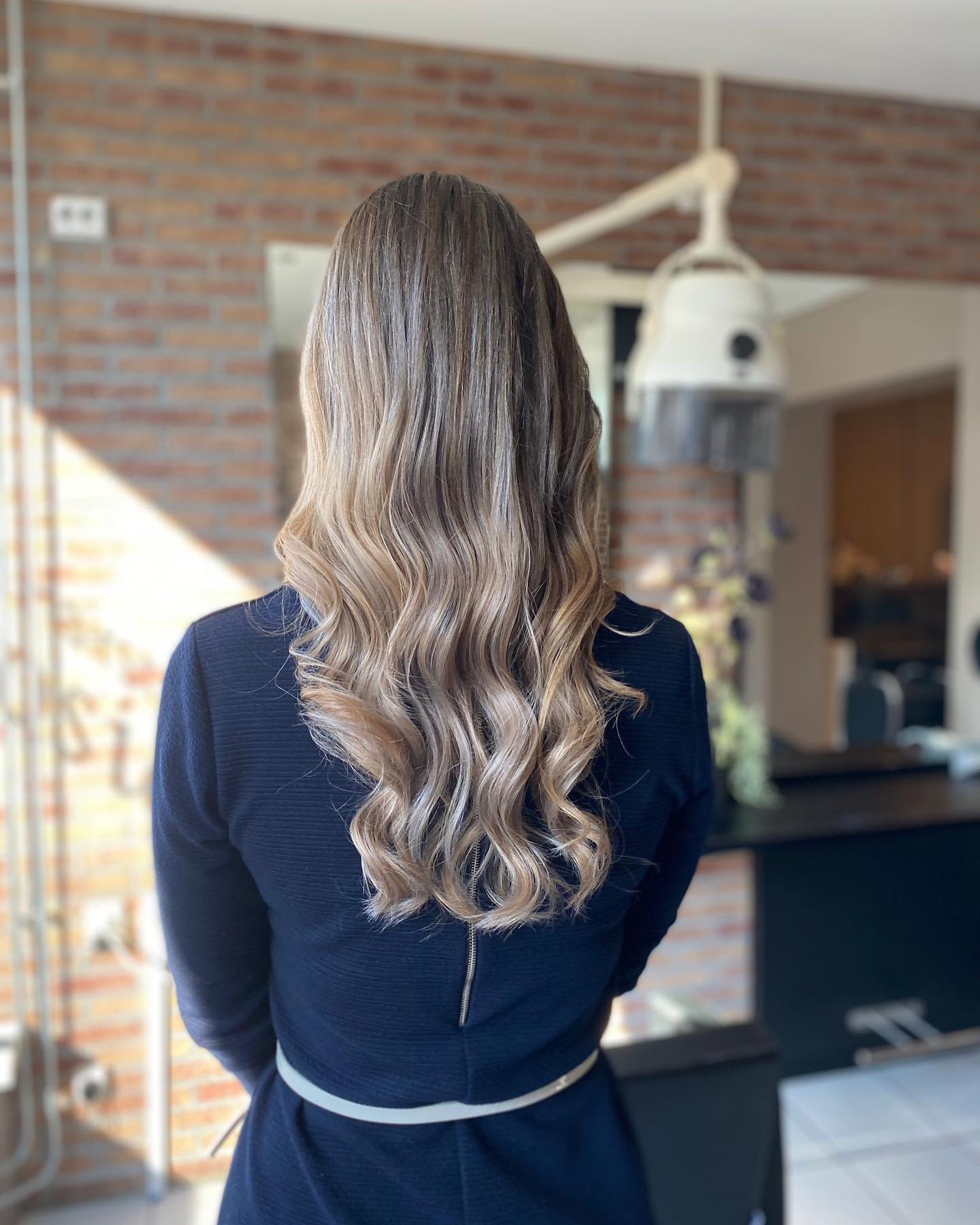 Lange golven die van donker naar blond verlopen, in de salon met de bakstenen muur